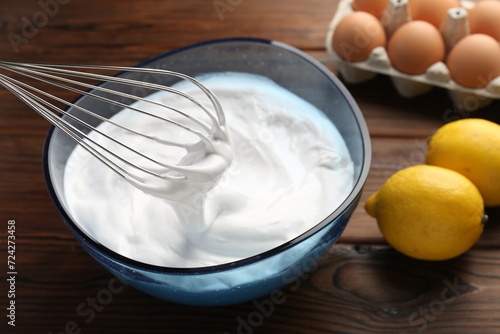 Bowl with whipped cream, whisk and ingredients on wooden table