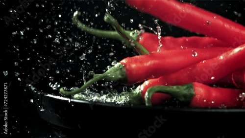 The chili peppers fall with splashes into the plate. On a black background. Filmed on a high-speed camera at 1000 fps. High quality FullHD footage photo
