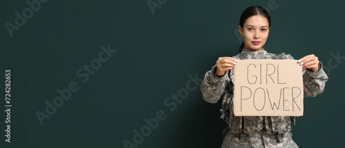 Young female soldier holding paper with slogan GRL PWR on dark background with space for text. Feminism concept photo