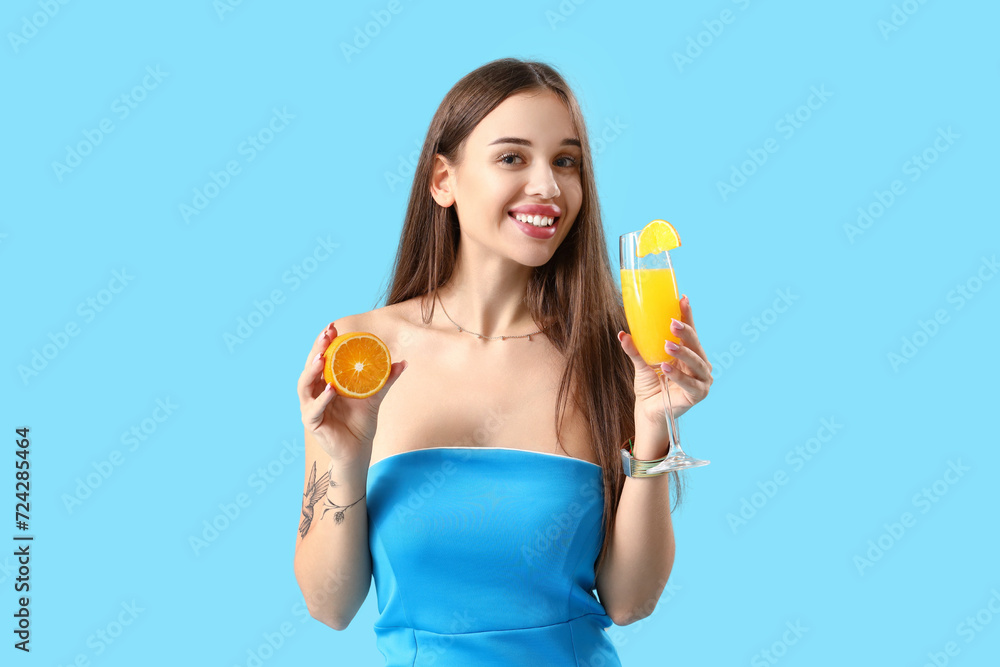 Beautiful young woman with glass of tasty citrus cocktail and orange piece on blue background Beautiful young woman with glass of tasty citrus cocktail and orange piece on blue background