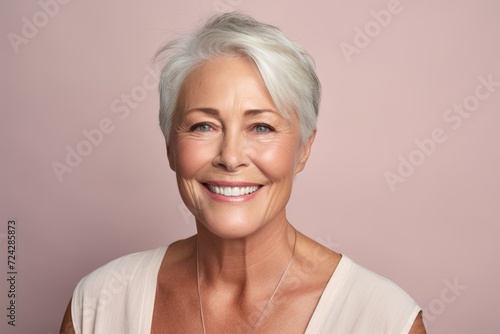 Portrait of smiling senior woman with white hair on pink background.