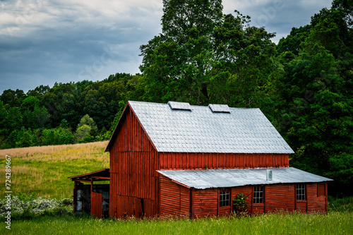 Rustic Red Barn in a Lush Green Field Under a Stormy Sky at Dusk