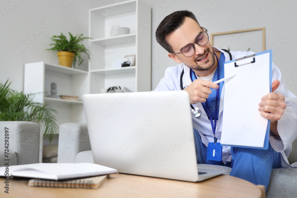 Handsome doctor showing clipboard to patient online at home Handsome doctor showing clipboard to patient online at home