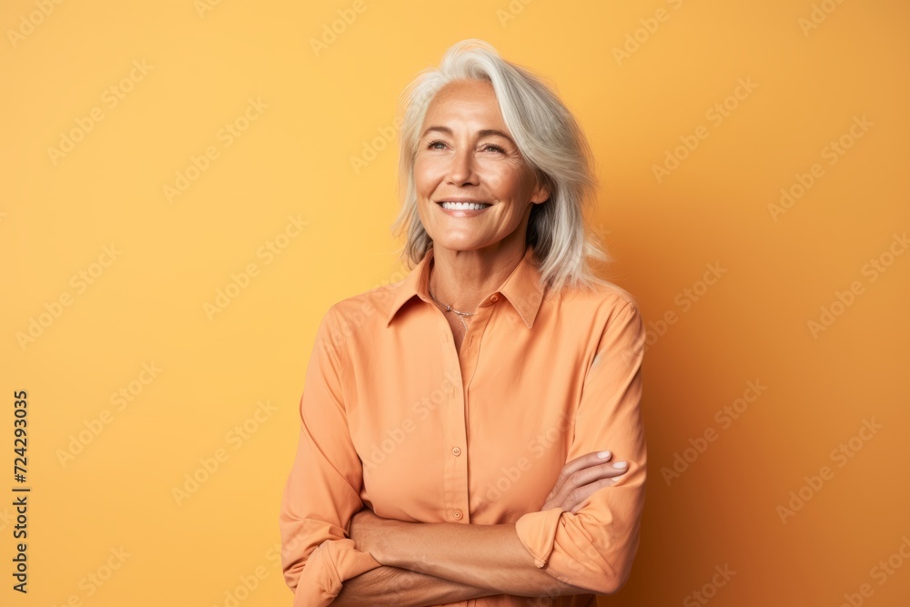 Portrait of smiling senior woman with crossed arms standing against yellow background Portrait of smiling senior woman with crossed arms standing against yellow background