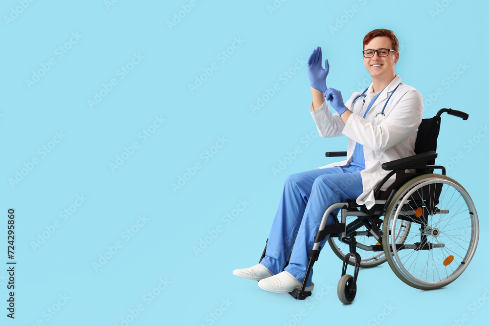 Male doctor in wheelchair putting medical gloves on blue background