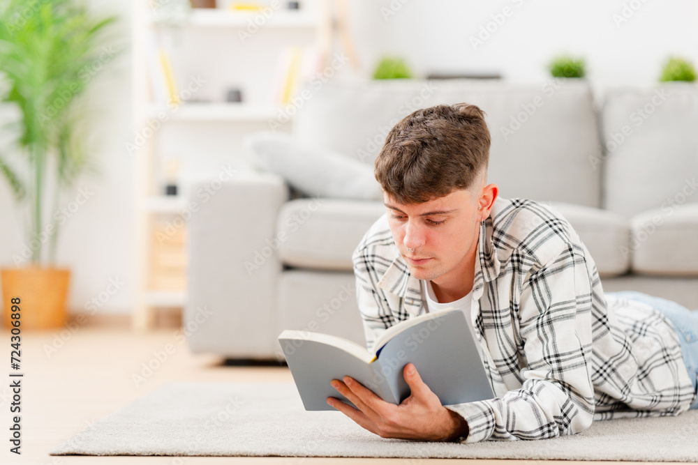 Young caucasian man studying lying on the floor. Person reading a book in the living room Young caucasian man studying lying on the floor. Person reading a book in the living room