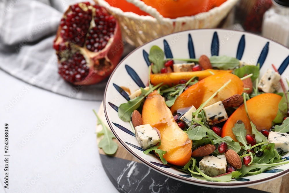 Tasty salad with persimmon, blue cheese, pomegranate and almonds served on white table, closeup. Space for text Tasty salad with persimmon, blue cheese, pomegranate and almonds served on white table, closeup. Space for text