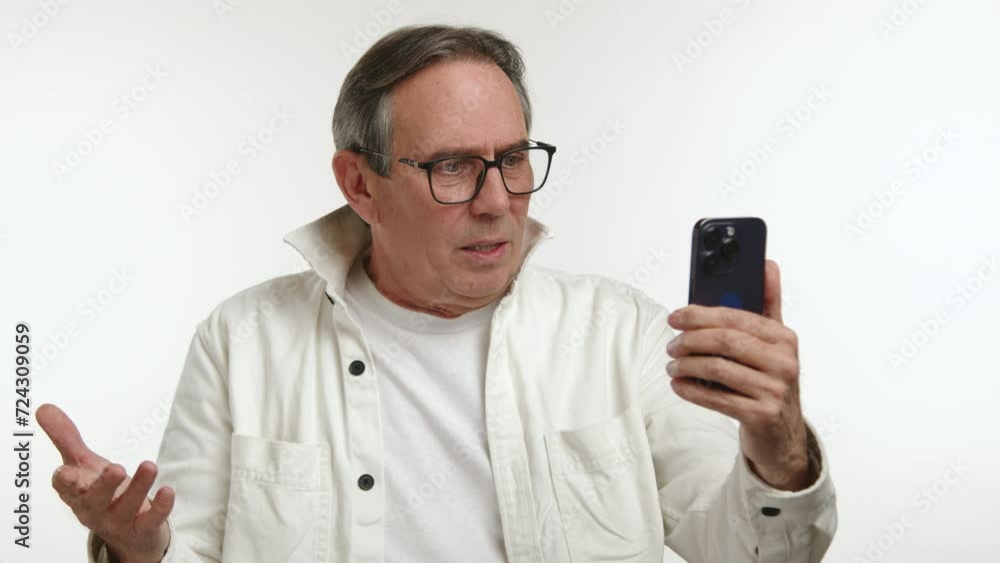 A senior man in a casual white jacket looks perplexed and somewhat frustrated as he tries to communicate over a video call, his expression showing a mix of concentration and confusion. Camera 8K RAW. A senior man in a casual white jacket looks perplexed and somewhat frustrated as he tries to communicate over a video call, his expression showing a mix of concentration and confusion. Camera 8K RAW.