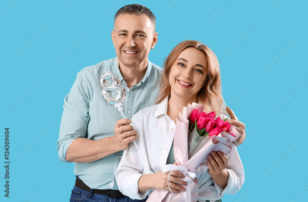 Middle-aged couple with bouquet and balloon in shape of figure 8 on blue background. International Women's Day Middle-aged couple with bouquet and balloon in shape of figure 8 on blue background. International Women's Day