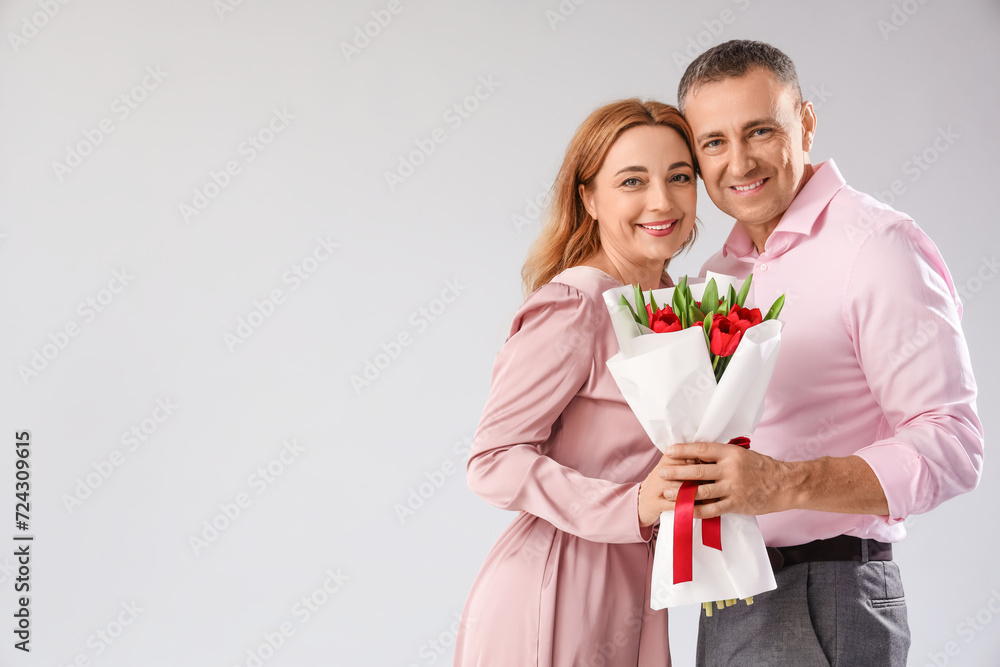 Middle-aged couple with bouquet of flowers on grey background. International Women's Day Middle-aged couple with bouquet of flowers on grey background. International Women's Day
