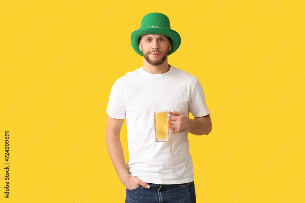 Young man in leprechaun hat with glass of beer on yellow background. St. Patrick's Day celebration