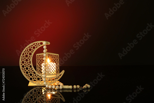Decorative crescent with burning candle and prayer beads for Ramadan on dark red background