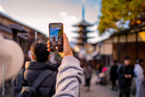 Yasaka Pagoda view and Hokan-ji Temple from Yasaka Dori street in Kyoto, Japan. Popular touristic street leading to Kyomizu Dera,Young female tourist taking photo with a mobile phone during sunset.