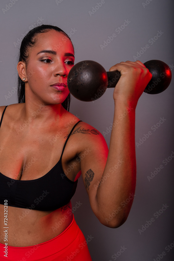 Beautiful brunette woman, in gym clothes, doing exercises with her arm holding black dumbbells. Healthy life.