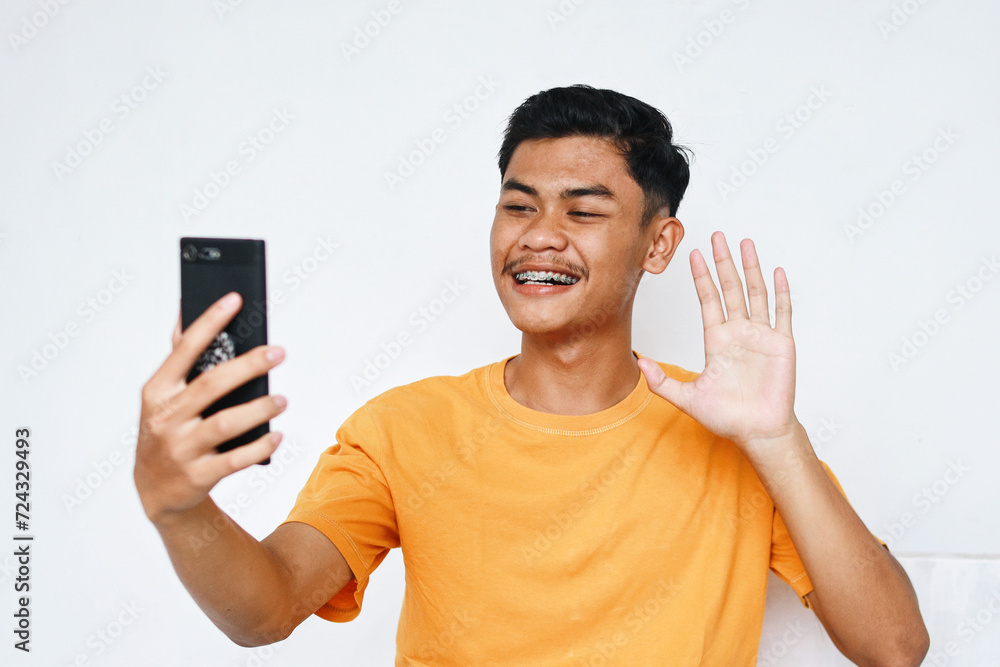 Young Asian student male with dental braces having video call on smartphone at home Young Asian student male with dental braces having video call on smartphone at home