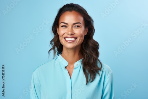 Portrait of happy smiling young woman in blue shirt, over blue background © Iigo