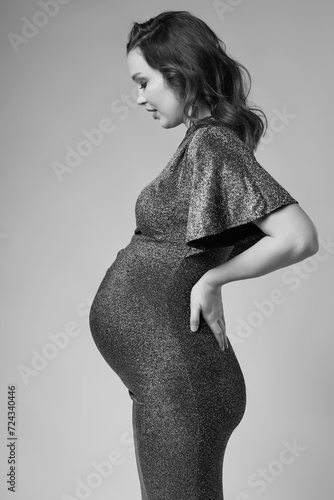 Black and white portrait of young pregnant female in grey sequin dress.