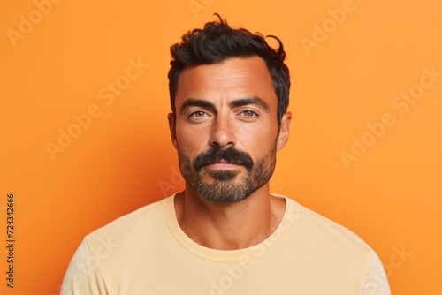Portrait of handsome man with beard and mustache looking at camera over orange background © Iigo