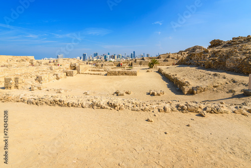 View of the ruins and excavations of the ancient Tylos Fort  a coastal fortress adjacent to Qal at al-Bahrain fort  with the modern skyline of Manama  Bahrain in the distance.