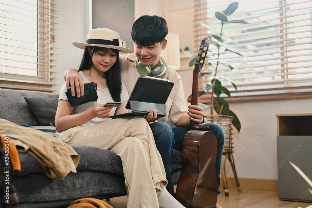 Happy young couple planning holiday trip, buy tickets, purchase flight or book hotel on digital tablet