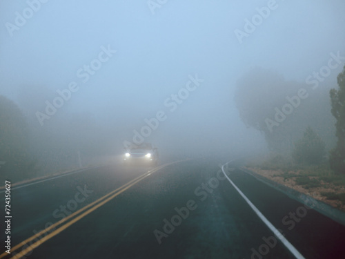 Lonely Car driving with headlights on a foggy road with low visibility 