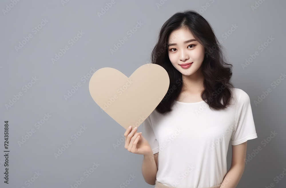 Photo of asian chinese girl with beautiful black hair, smiling and keeping pink paper heart shaped invitation card, looking at copyspace isolated on pastel pink color background Photo of asian chinese girl with beautiful black hair, smiling and keeping pink paper heart shaped invitation card, looking at copyspace isolated on pastel pink color background