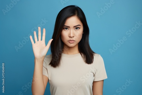 Young woman on a blue studio backdrop standing with outstretched hand showing stop sign Generative AI © Tony