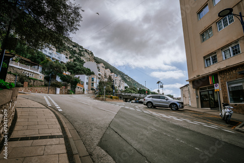 Gibraltar, Britain - January 24, 2024 - street with parked cars, buildings, and a hill in the background under a cloudy sky.