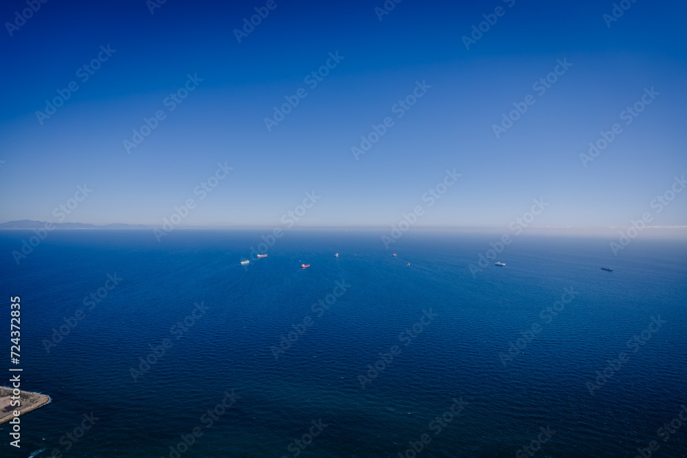 Fototapeta premium Gibraltar, Britain - January 24, 2024 - clear blue sea with several ships and a distant mountain range under a bright blue sky.