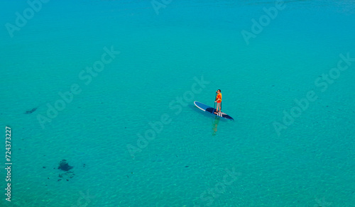 Happy Asian young man standing on a sup Surfing balancing on supboard paddling with water sea background