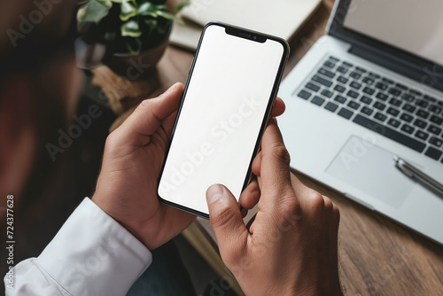 Cropped shot of businessman using smartphone with blank screen while sitting at modern office desk