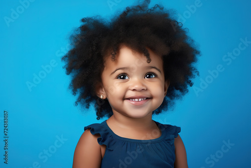 A joyful toddler with a charming smile and a stylish jheri curl hairstyle gazes into the camera, showcasing her innocent beauty and youth in this captivating portrait