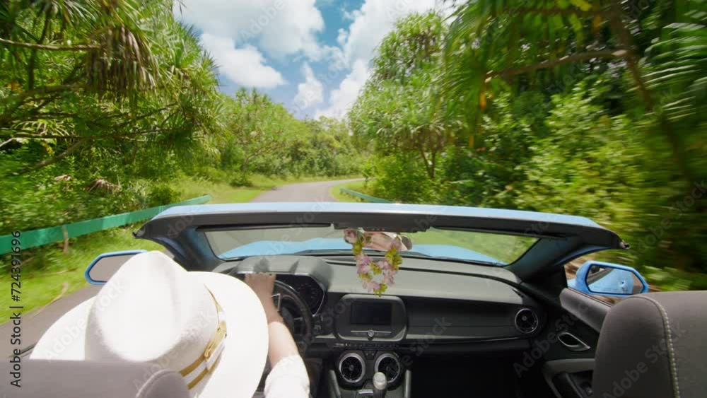 Woman in white hat feeling free while driving car. Summer travel adventure. Happy traveler singing and dancing, waving hand while exploring tropical garden on Hawaii island in cabriolet without roof Woman in white hat feeling free while driving car. Summer travel adventure. Happy traveler singing and dancing, waving hand while exploring tropical garden on Hawaii island in cabriolet without roof