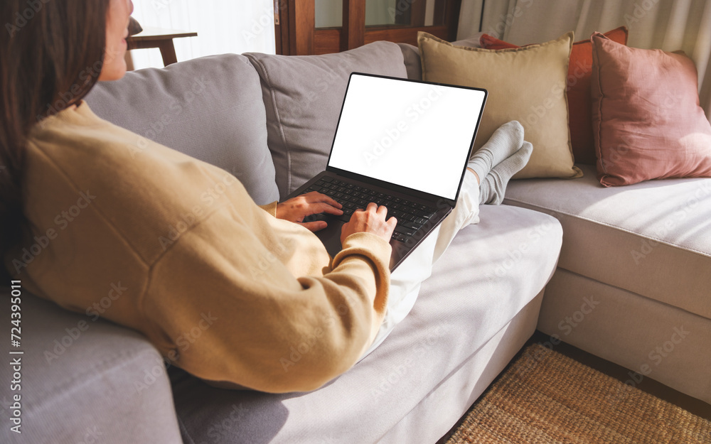 Mockup image of a woman working and typing on laptop computer with blank screen while sitting on sofa at home Mockup image of a woman working and typing on laptop computer with blank screen while sitting on sofa at home