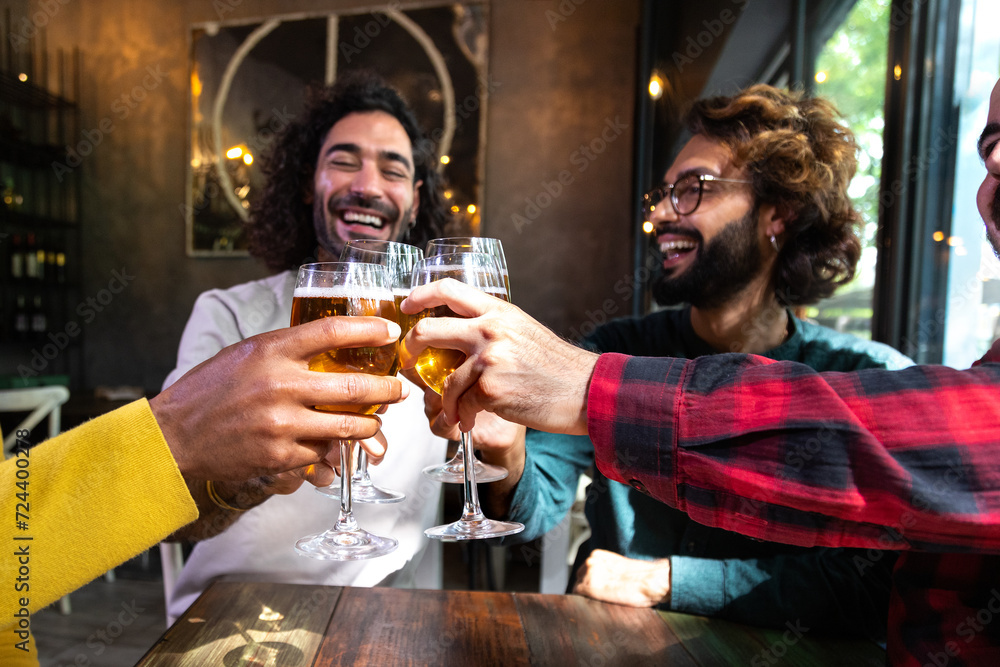 Happy male friends in a bar enjoying drinks together toasting with beer, having fun.