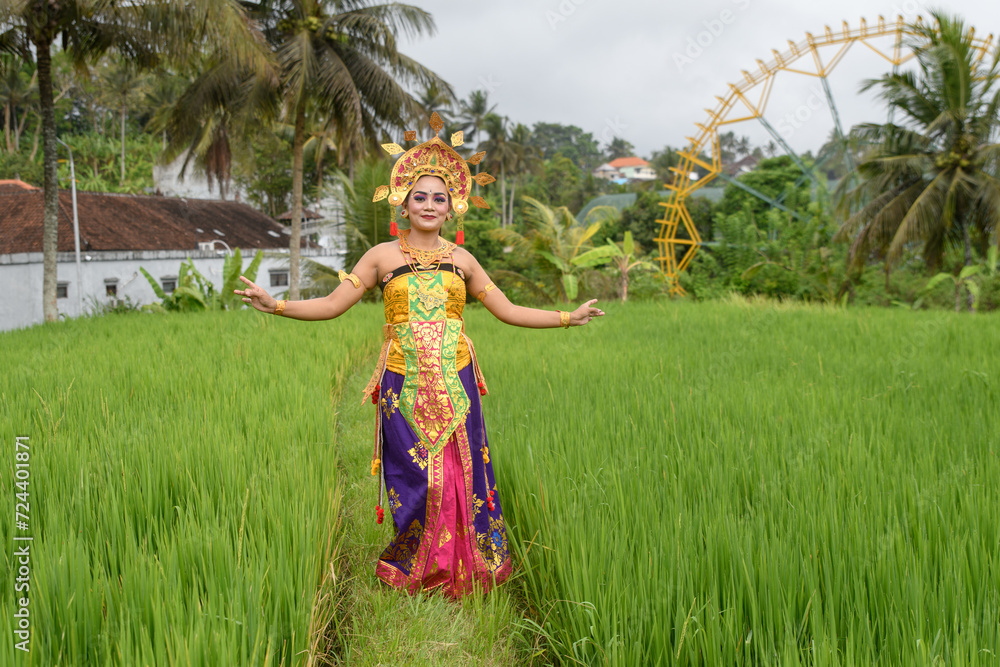 Amidst nature, a woman Bali dancer adorned in colorful traditional dress strikes a pose. Amidst nature, a woman Bali dancer adorned in colorful traditional dress strikes a pose.