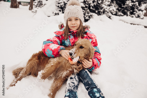  A girl plays in the snow with a dog in winter. Beautiful red dog, beautiful girl.