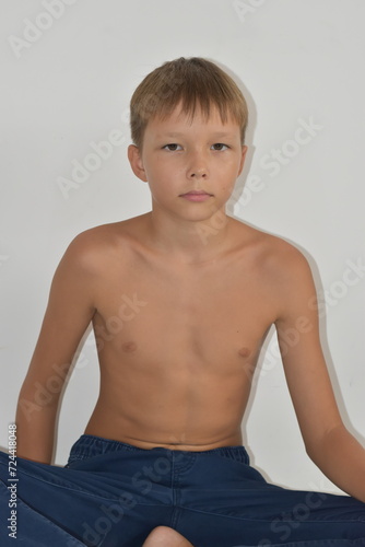 A fair-haired boy sits in blue jeans without a shirt.