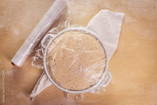 Yeast dough covered by plastic wrap, proofed dough for baking bread or pizza