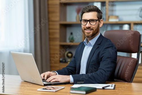 Smiling attractive man in stylish suit holding hands on pc keyboard and confidently looking at camera. Successful employee feeling satisfied about working in company and personal career achievements.
