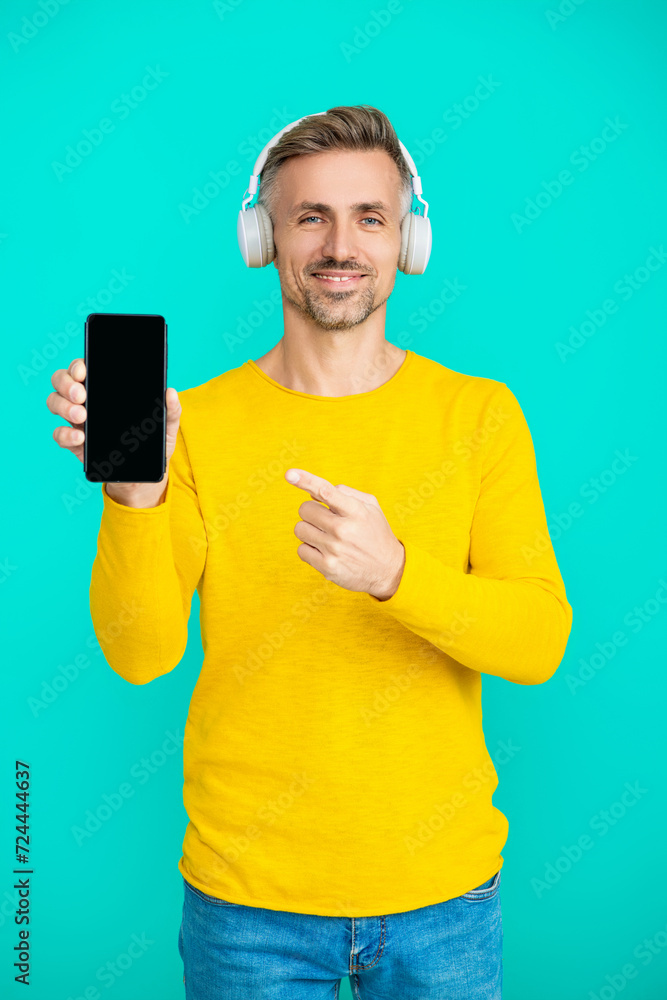 Point finger on phone screen. Music lifestyle. Audio playlist. Mature man in headphones. Man in headphones choosing playlist of mp3 on phone. Man using phone application isolated in blue. Copy space Point finger on phone screen. Music lifestyle. Audio playlist. Mature man in headphones. Man in headphones choosing playlist of mp3 on phone. Man using phone application isolated in blue. Copy space