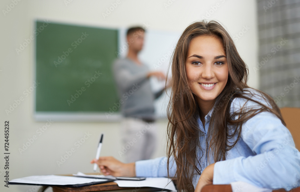 Woman, portrait and writing or learning in classroom for education, language development or teaching knowledge. Face of happy student at her desk for high school, notebook and test notes with teacher Woman, portrait and writing or learning in classroom for education, language development or teaching knowledge. Face of happy student at her desk for high school, notebook and test notes with teacher