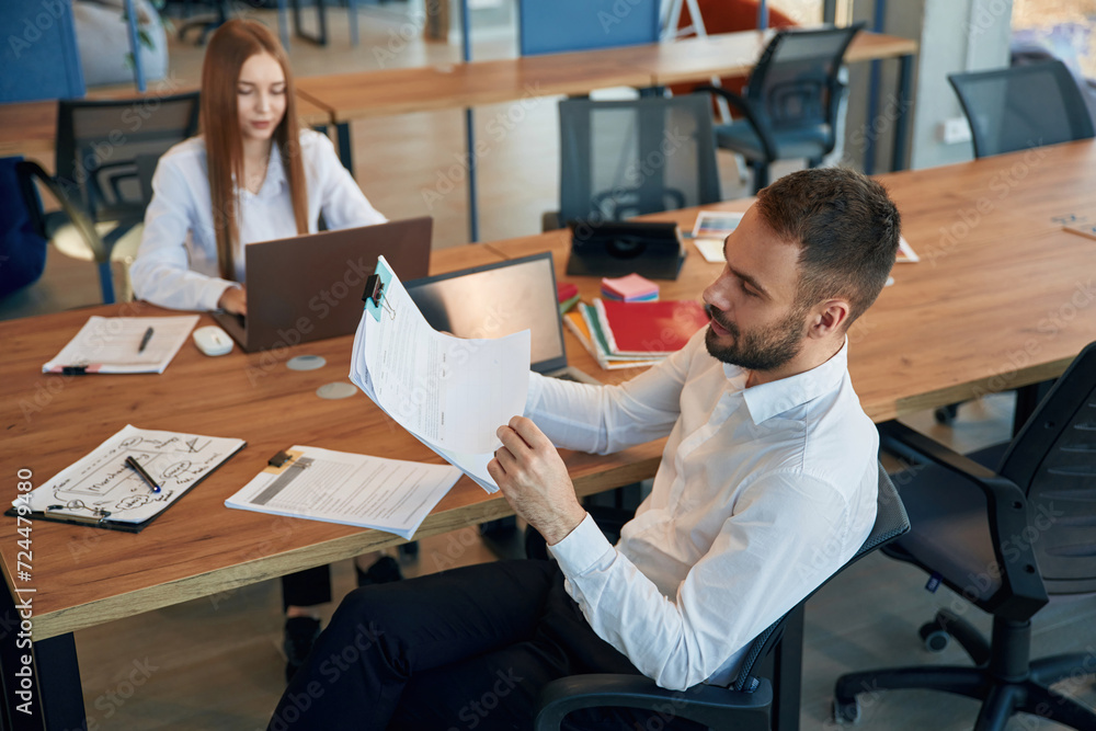 Sitting by the table. Man and woman employees are working in the office Sitting by the table. Man and woman employees are working in the office