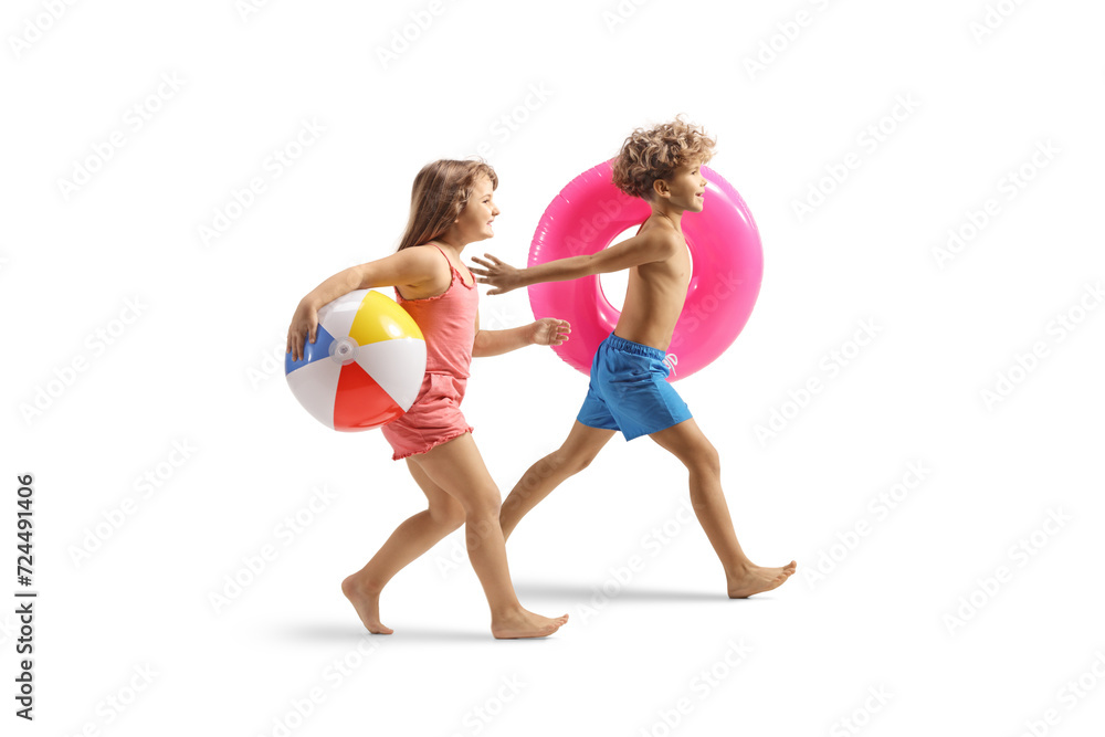 Playful kids in swimwear running and carrying a swimming ring and a ball - obrazy, fototapety, plakaty 