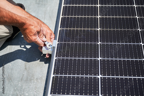 Worker building photovoltaic solar panel system on rooftop of house. Close up of man engineer installing solar module with help of wrench outdoors. Alternative and renewable energy generation concept.