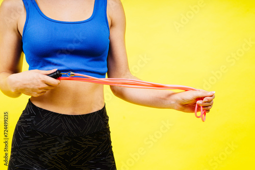 Fit female athlete with ponytail jumping with rope during fitness training against yellow background