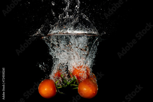A bunch of tomatoes falling into water with a black background creating bubbles and a splash