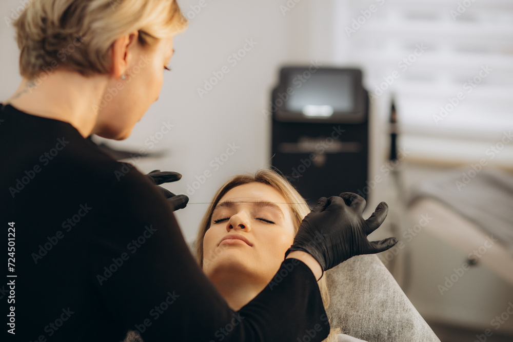 Young woman having eyebrow correction procedure in beauty salon - obrazy, fototapety, plakaty 