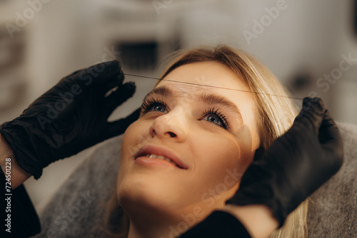 The girl beautician marks with the help of thread eyebrow tattoo. Permanent makeup. Permanent tattooing of eyebrows.