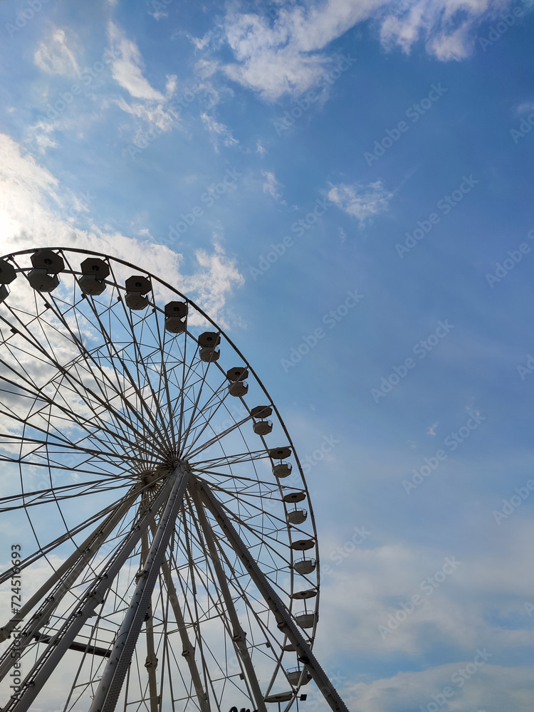 Part of large Ferris wheel against the background of summer  daytime blue sky with clouds. Empty booths, no people. Attraction. Entertainment. Pastime. Vacation. Tourism. Copy space. Selective focus.